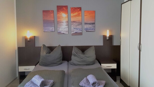 Quarto de hotel com duas camas, um guarda-roupa e três quadros de pôr do sol na parede.