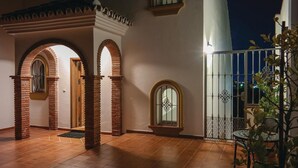 Un cortile con archi in mattoni, pavimento piastrellato e un'area recintata con tavolo e sedie.