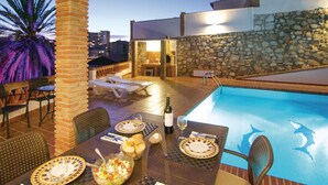 Area piscina sul tetto con tavolo da pranzo per due persone, una bottiglia di vino e una ciotola di frutta.