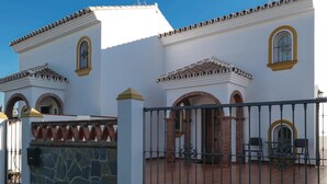 Un edificio a due piani con pareti bianche e tegole in terracotta. Sono presenti due finestre ad arco e un balcone con ringhiere in metallo.