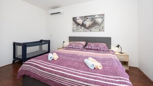 Un dormitorio con cama, cabecera, aire acondicionado de pared, mesita de noche, lámpara y un cuadro.