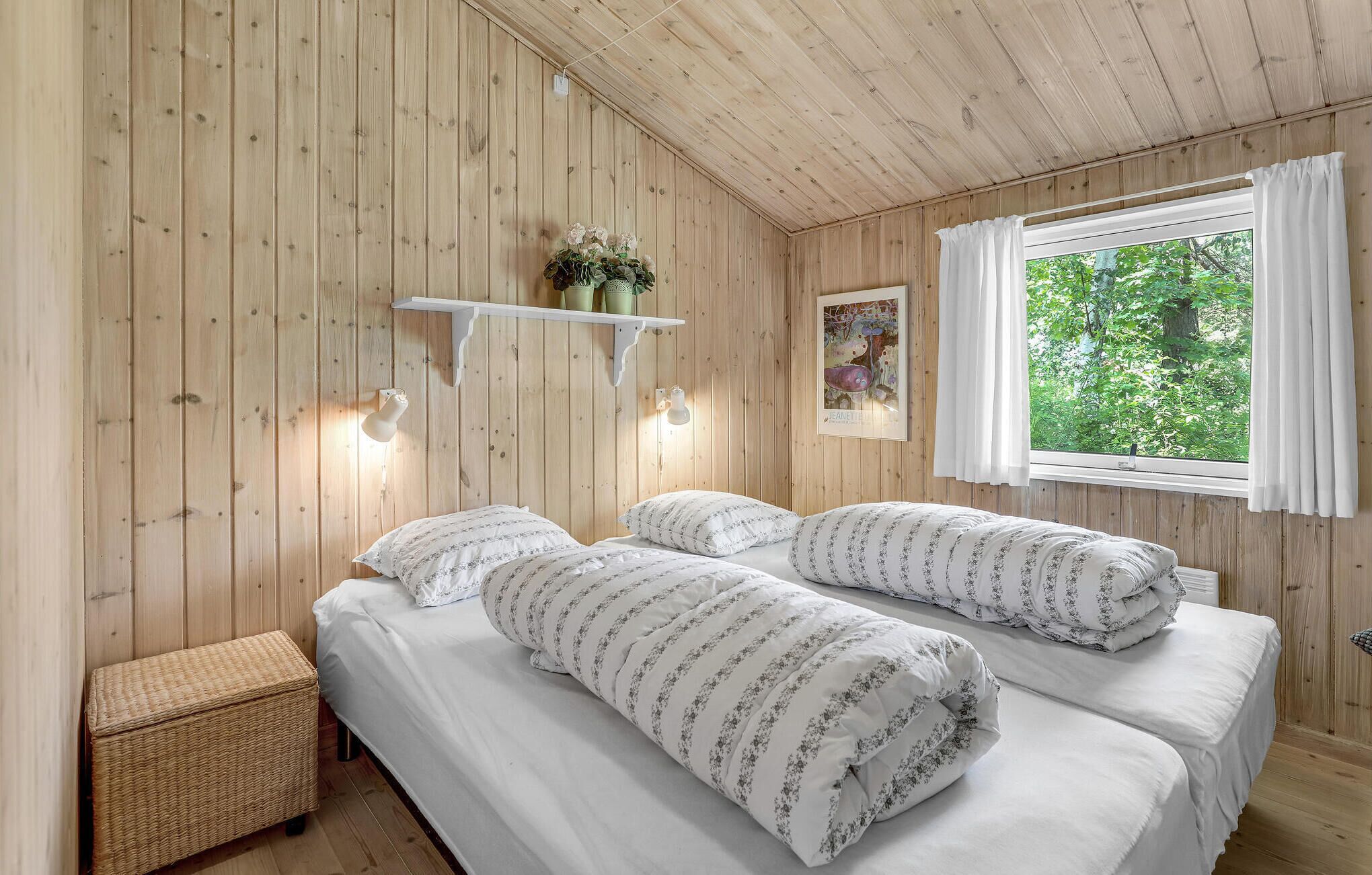 Ett sovrum med träpanel på väggarna, två sängar, ett fönster med gardiner, en vägghylla med dekorativa föremål och en liten bänk.