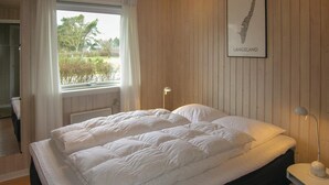 A neatly made bed with white bedding in a room with wooden paneling, a window with a view of greenery, and a framed map on the wall. - Nice home in Rudkøbing with WiFi (Rudkøbing)