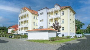 Ein mehrgeschossiges Wohngebäude mit Balkonen, einem überdachten Eingang und einem gepflasterten Auffahrt.