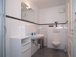 A modern bathroom with a white sink, mirror, and toilet. There are storage cabinets and a trash can.