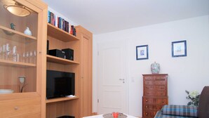 Ein gemütlicher Wohnraum mit einer Holzregal, einem Fernseher, einem kleinen Tisch mit Spitze und einem Schlafsofa sowie einer Kommode.