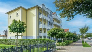 Ein mehrgeschossiges Gebäude mit Balkonen, einem gepflasterten Weg und Grünflächen.