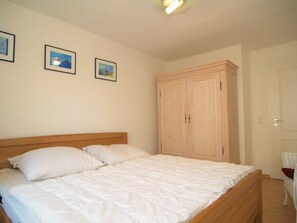 A bedroom with a wooden bed, white bedding, and a wardrobe.