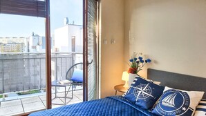 Een slaapkamer met een groot bed, uitzicht op de stad vanaf een balkon en kussens met een nautisch thema.