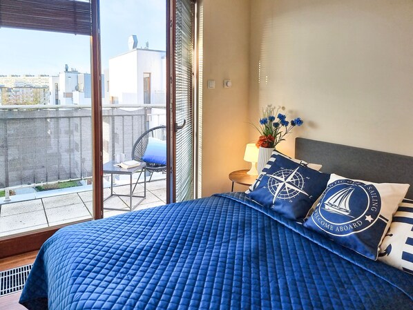 A bedroom with a large bed, a view of the city through a balcony, and nautical-themed pillows.