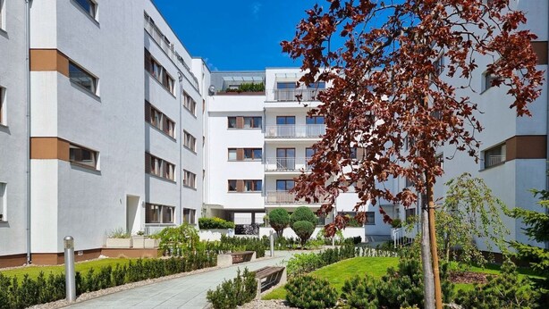 Een modern appartementencomplex met meerdere balkons, een verzorgde tuin en een helderblauwe lucht.