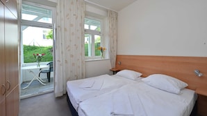 Ett sovrum med två sängar, en sänggavel i trä, ett fönster med gardiner, ett litet bord med en vas med blommor och utsikt över en trädgård utanför.