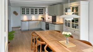 A modern kitchen with white cabinets, a wooden dining table, and a vase of flowers.
