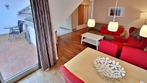 A modern living room with a sofa, a coffee table, and a dining table. There is a balcony with a table and chairs outside. - Apartment Perlmuschel (A) - Villa Ahlbeck House 2 (Heringsdorf)