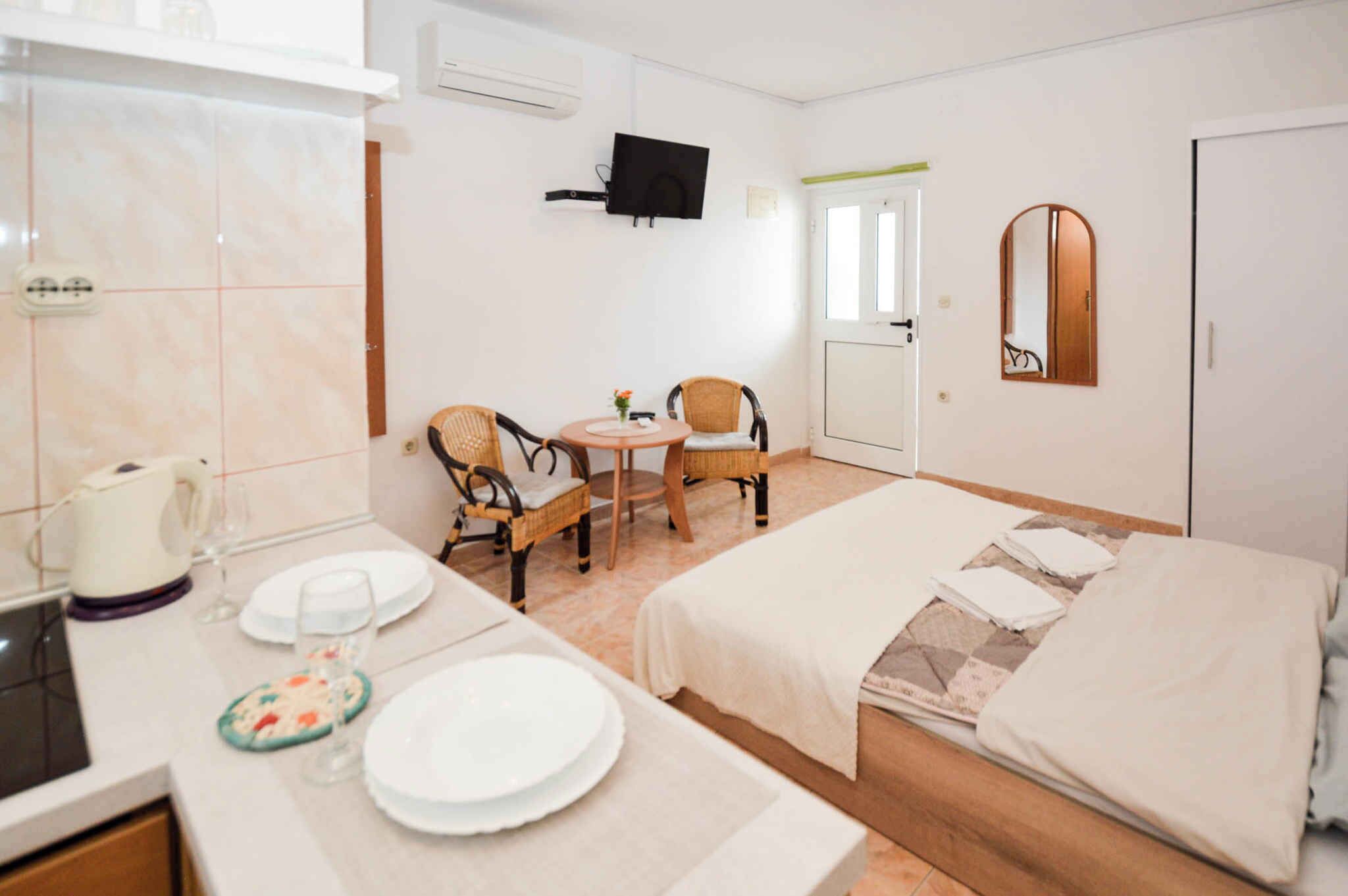 A hotel room with a bed, a small dining table with chairs, a TV mounted on the wall, and a mirror.