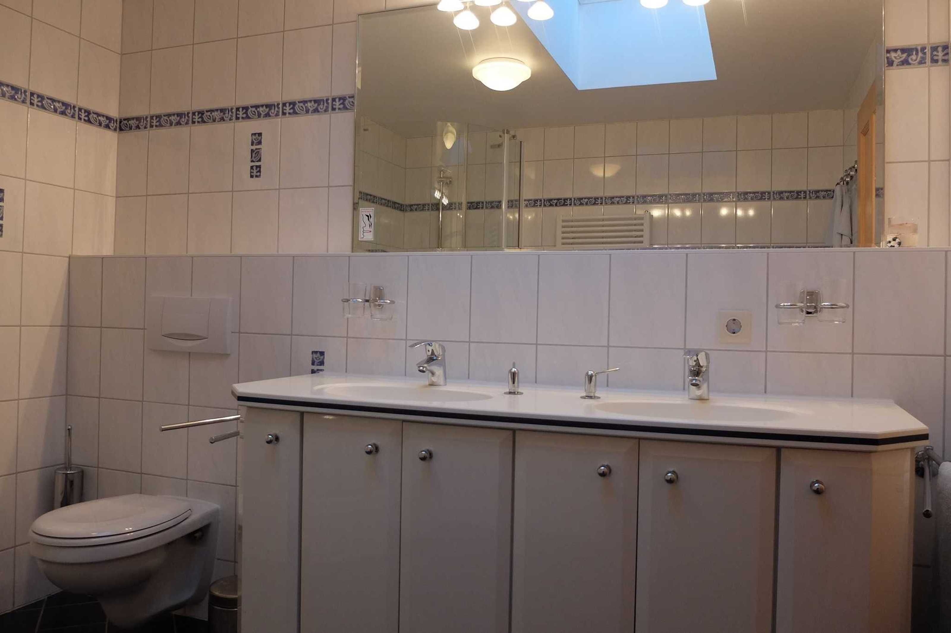 Un bagno con un lavandino bianco, due rubinetti, uno specchio e un water.