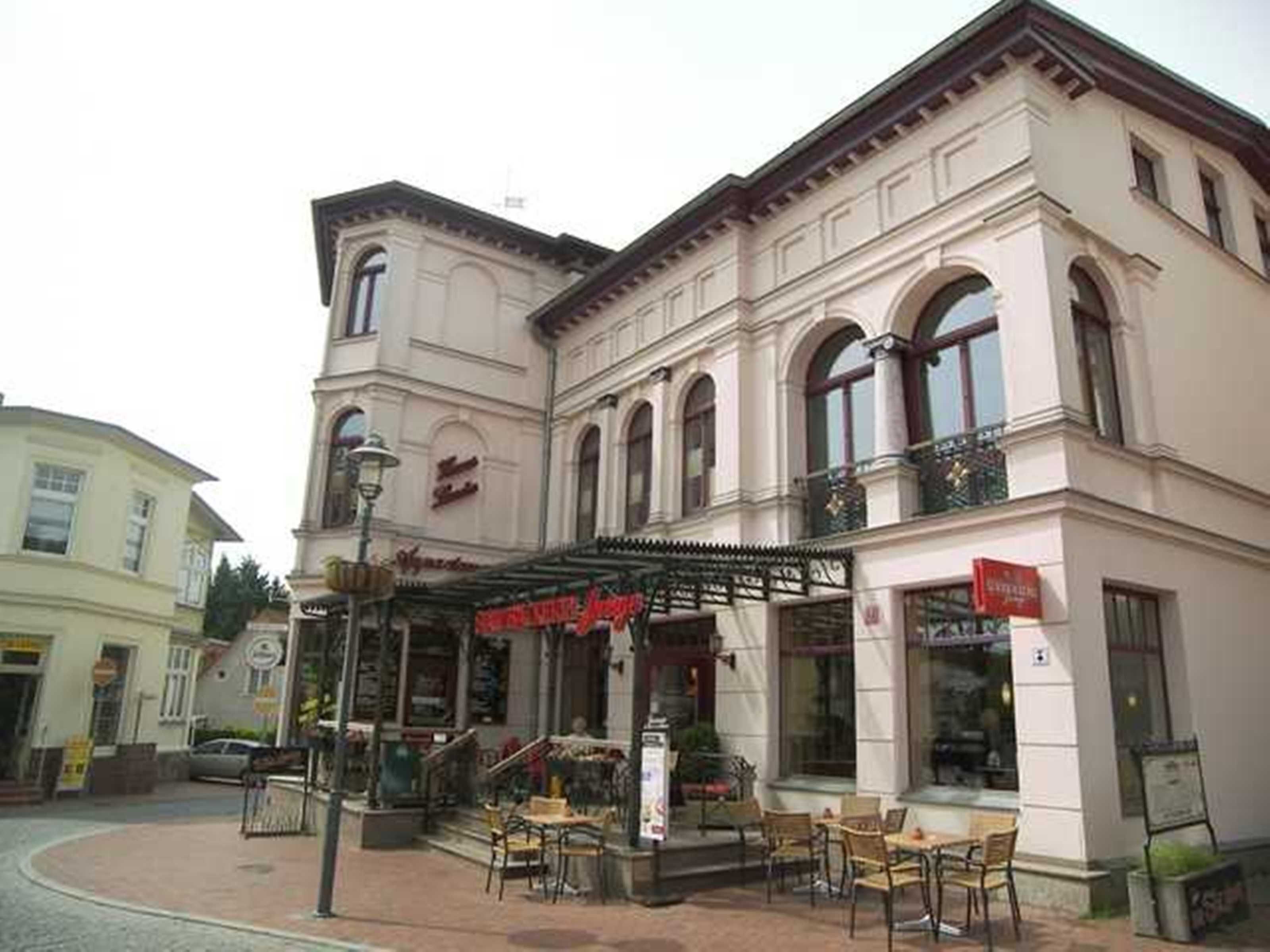 A building with a cafe on the ground floor, featuring outdoor seating and a staircase leading to the upper floor.