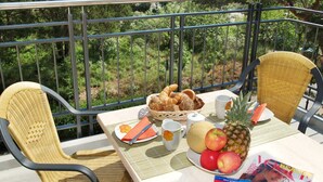 Un balcon avec des fauteuils en osier, une table avec des éléments pour le petit-déjeuner et un magazine.