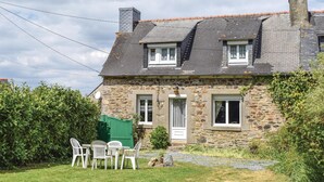 A stone house with a sloped roof, two windows, a door, and a small garden with a table and chairs. - Lovely home in Le Faouet with kitchen (Le Faouet)