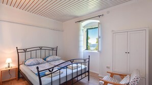 A bedroom with a bed, a nightstand, a chair, a window, and a door.