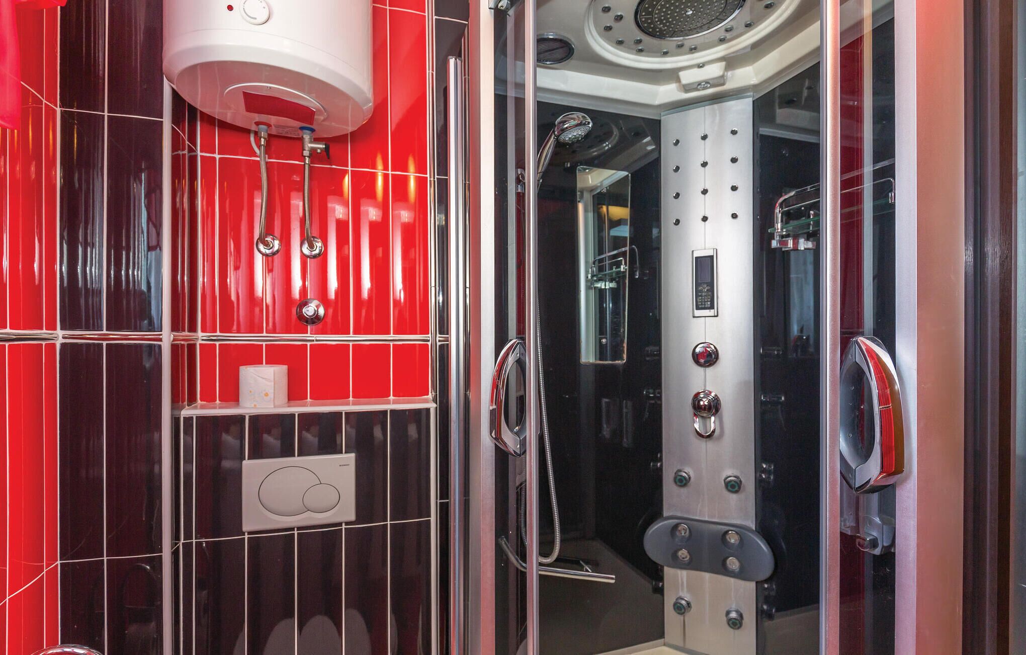 Un baño moderno con una cabina de ducha con azulejos rojos, un inodoro blanco y un panel de control visible.