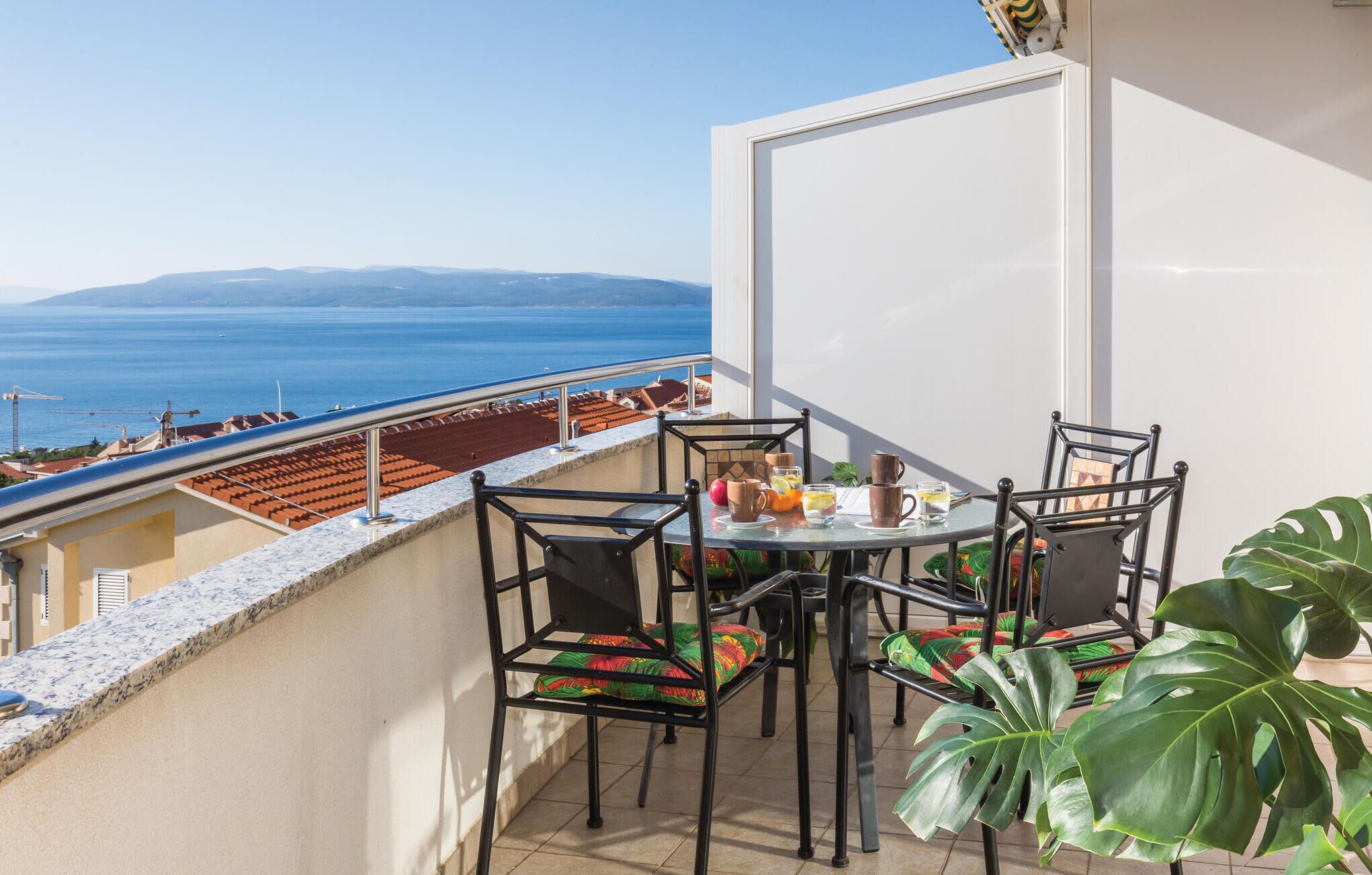 Ein Balkon mit Tisch und Stühlen, der Blick geht auf die Küste mit Gebäuden und dem Meer.