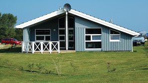 Een laag gebouw met een zadeldak, grote ramen en een witte veranda met een hekwerk.