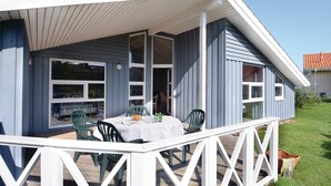 Een overdekt buitengebied met een tafel, stoelen, een witte balustrade en uitzicht op een huis met een rood dak.