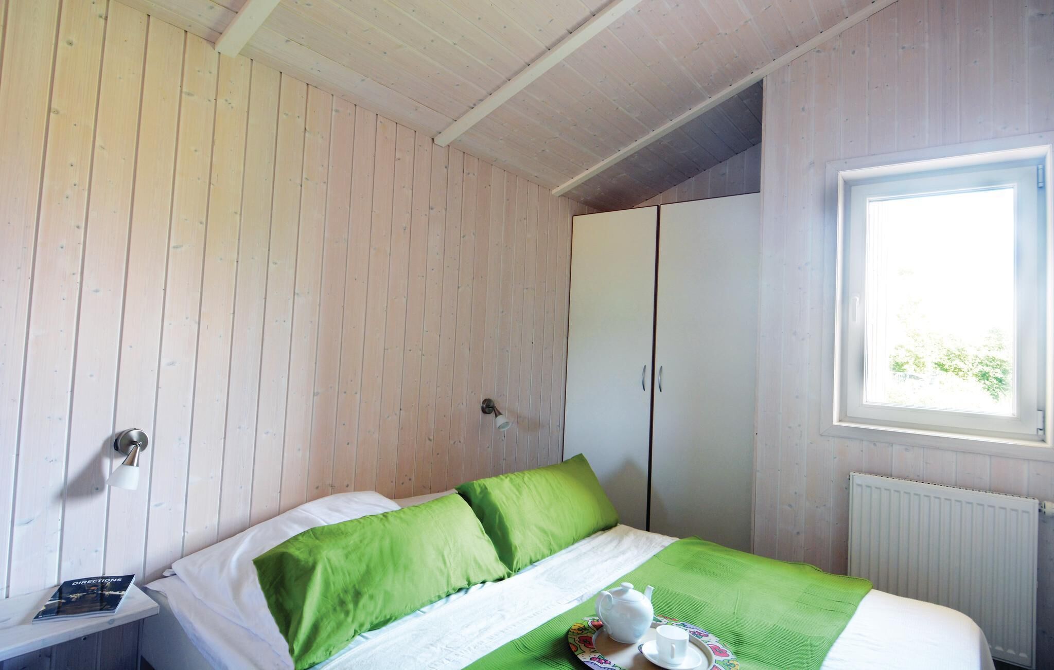 Een slaapkamer met een bed, een raam, een radiator en een kledingkast.