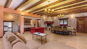 A spacious living area with a stone fireplace, a red sofa, a dining table set for four, and exposed wooden beams on the ceiling. - Pet friendly home in Visnjan (Visnjan)