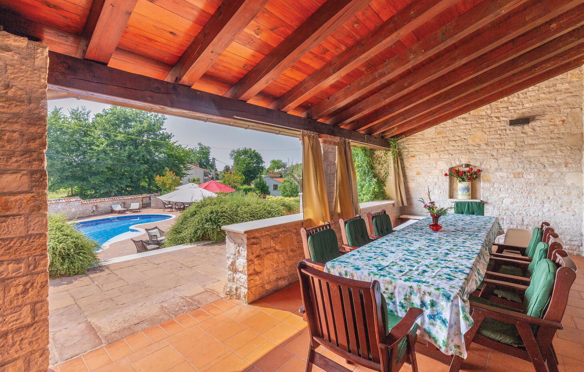 A covered outdoor dining area with a pool view, stone walls, and wooden furniture.