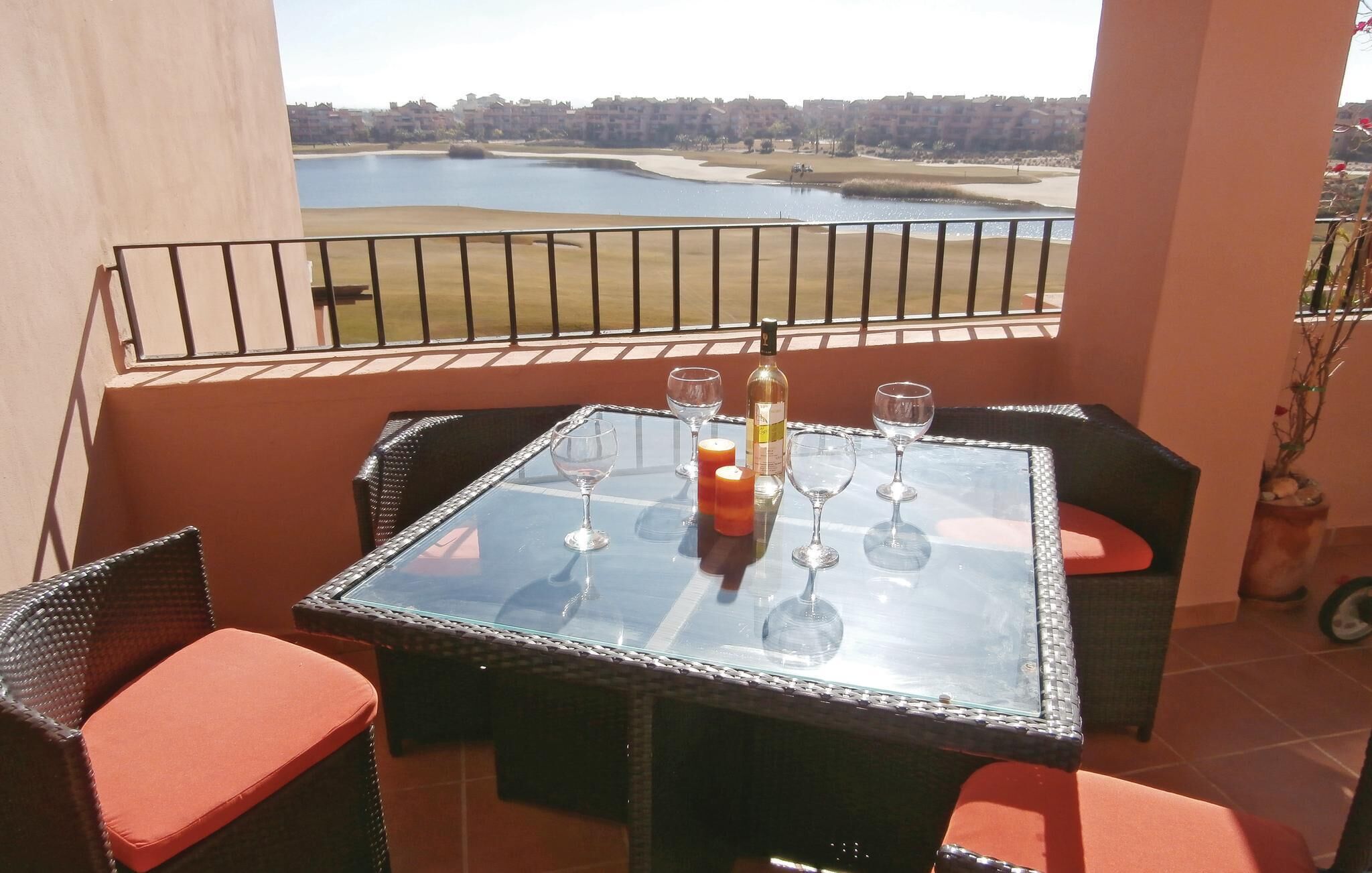 A balcony with a glass table, two chairs, and a bottle of wine.