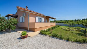 Ein zweistöckiges Haus mit roten Ziegeln, weißen Fensterläden und einem kleinen Garten mit Kies und Pflanzen.