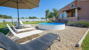 Ein Schwimmbecken mit Liegestühlen und einem Sonnenschirm, umgeben von Kieselsteinen und Pflanzen.