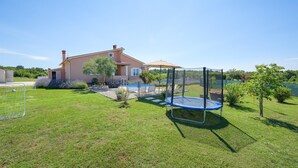 Ein Haus mit einem Garten, der einen Trampolin, ein kleines Schwimmbecken und eine Grünfläche umfasst.