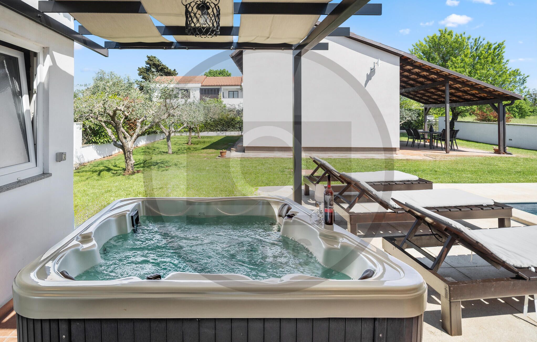 A hot tub with lounge chairs, a pergola, and a view of a residential area.