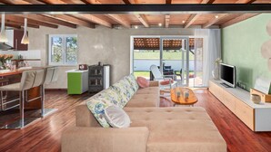 A modern living room with a sofa, coffee table, and TV area. There is a kitchen area with a dining table and chairs. The room has large windows and a view of the outdoors. - Beach front home in Valbandon (Valbandon)