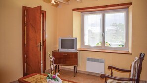Una habitación con puerta de madera, televisor sobre un mueble de madera, ventana con vidrio esmerilado y un radiador.