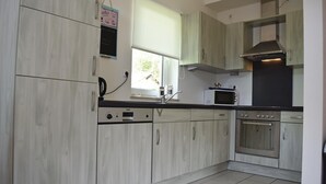 Una cucina moderna con mobili in legno chiaro, forno integrato, microonde e una finestra con vista sul verde.