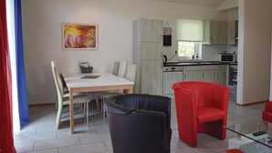 Una cucina moderna con mobili chiari in legno, un'area pranzo con tavolo e sedie bianche, e una sedia rossa.