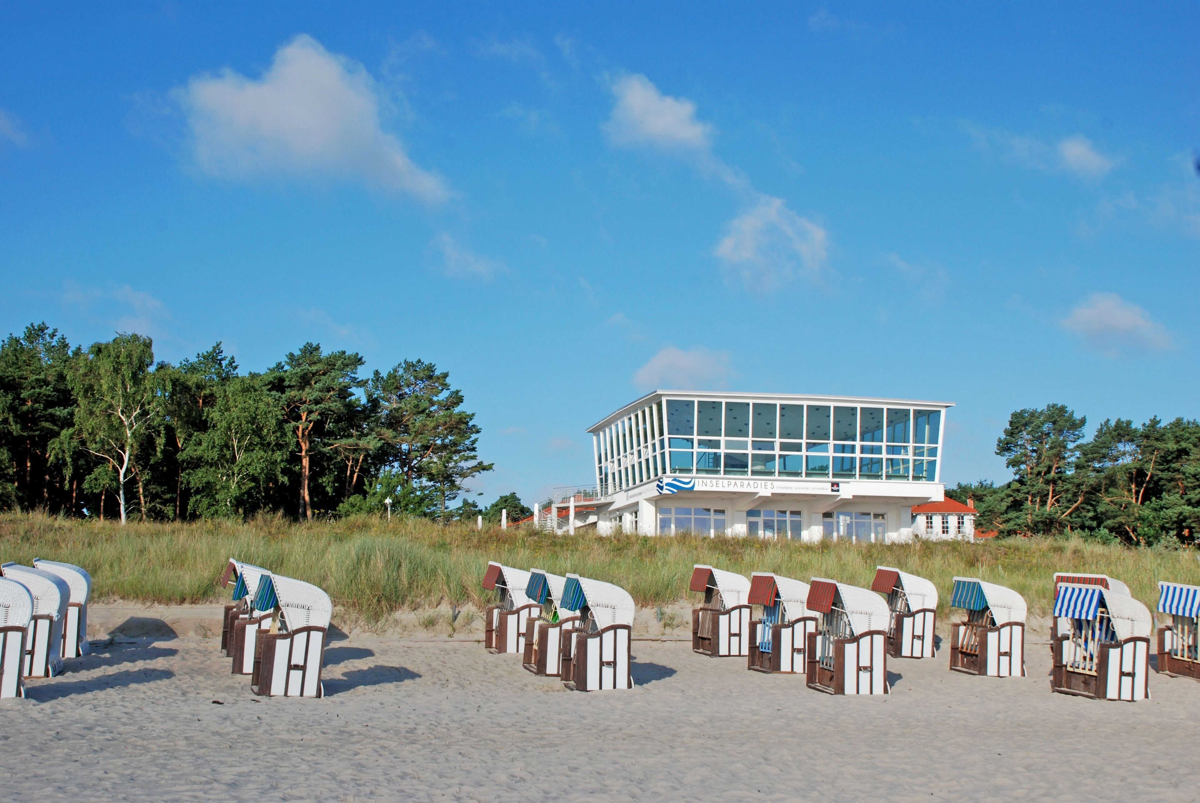 Een gebouw aan het strand met een modern ontwerp, rijen strandstoelen en een helder uitzicht op de oceaan.