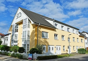 A multi-story residential building with a yellow facade, white trim, and multiple windows.