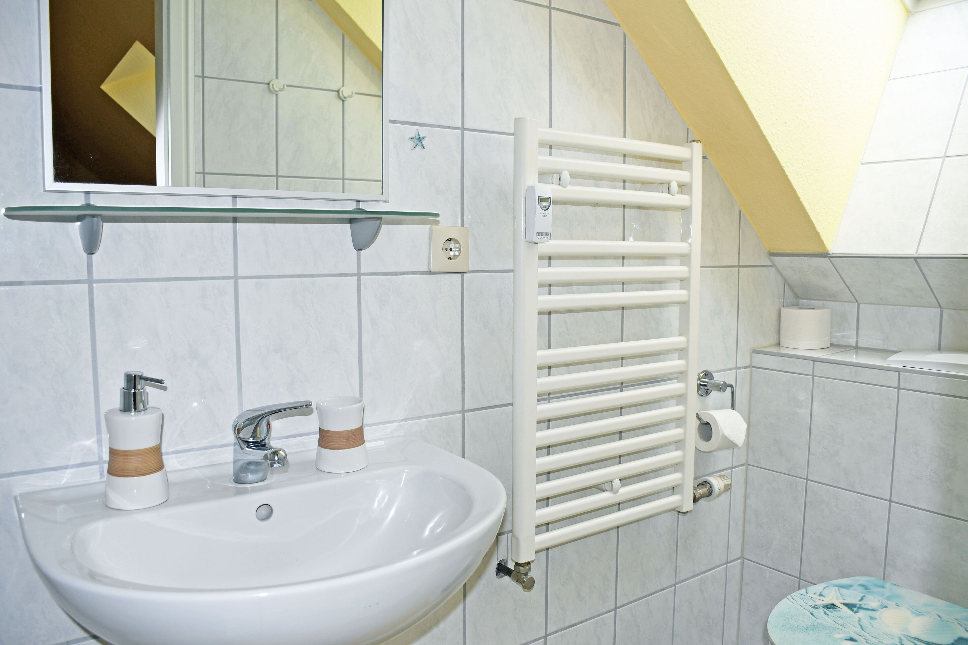 Un baño con lavamanos blanco, espejo y barra para toallas.