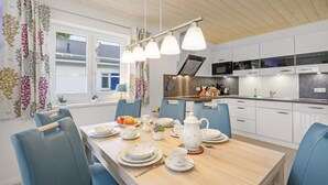 Una cucina moderna con mobili bianchi, un tavolo da pranzo in legno apparecchiato per quattro persone e vista all'esterno attraverso una finestra con tende.
