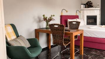 A modern bedroom with a bed, a table with chairs, a fireplace, and a green armchair.