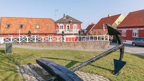 A red building with a white fence in front, a stone wall, and a sculpture of a fish. - 2 bedroom stunning apartment in Gudhjem (Gudhjem)