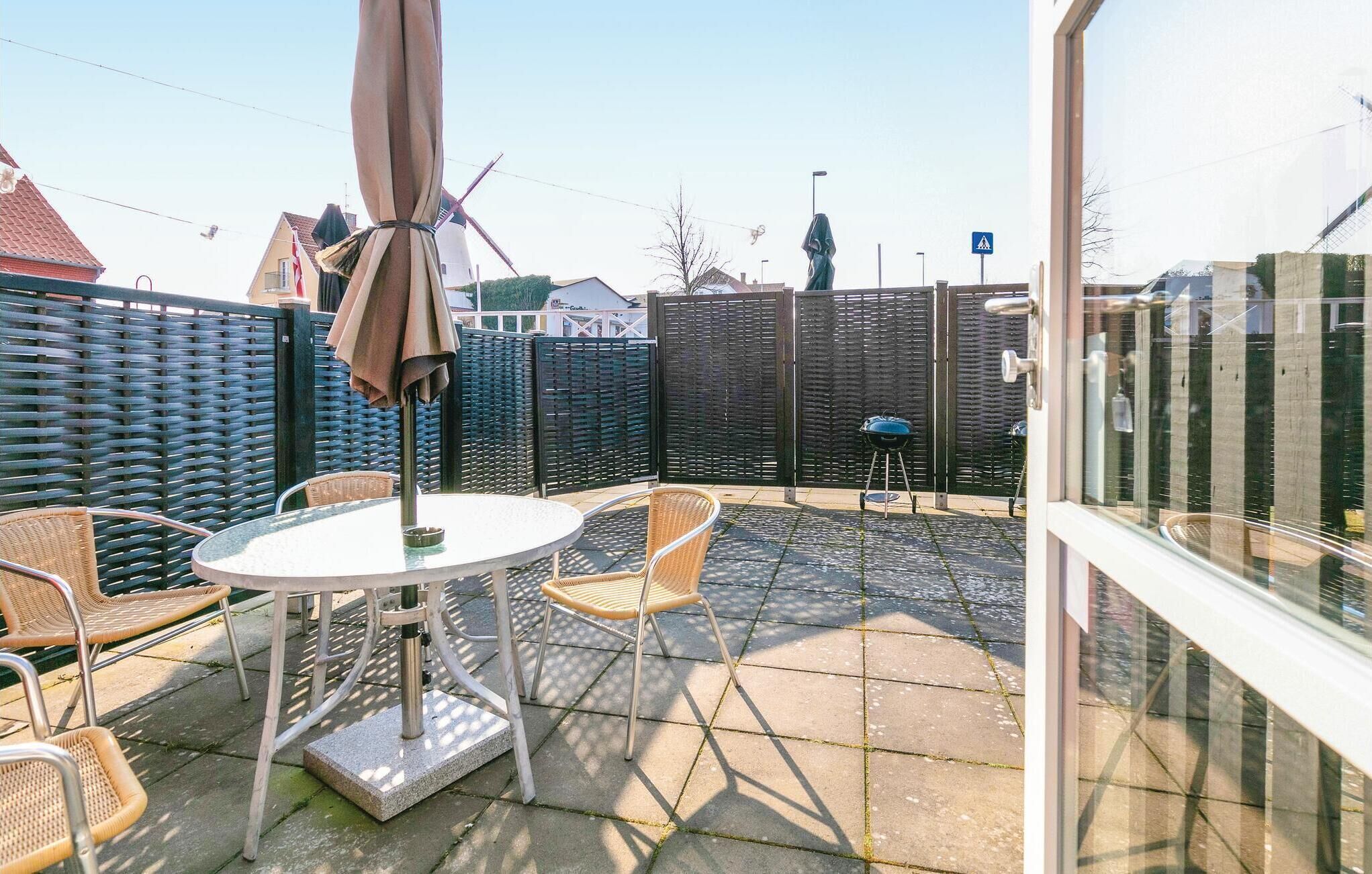 Eine Terrasse mit einem runden Tisch und Stühlen, einem Sonnenschirm und einem hohen Zaun.
