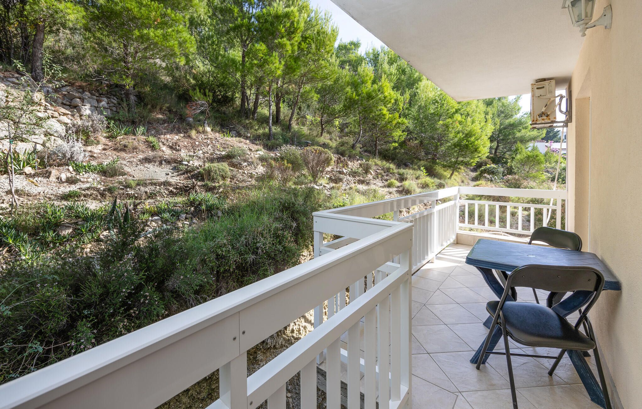 A balcony with a white railing, a table, and two chairs.