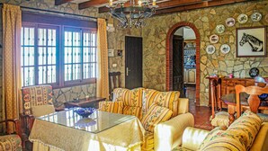 Ein gemütliches Wohnzimmer mit einer Steinwand, einer Chandelüster und einem Essbereich mit Holztisch und -stühlen.