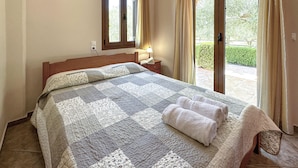 Un dormitorio con una cama, una mesita de noche, una ventana y una puerta que da a un espacio exterior.